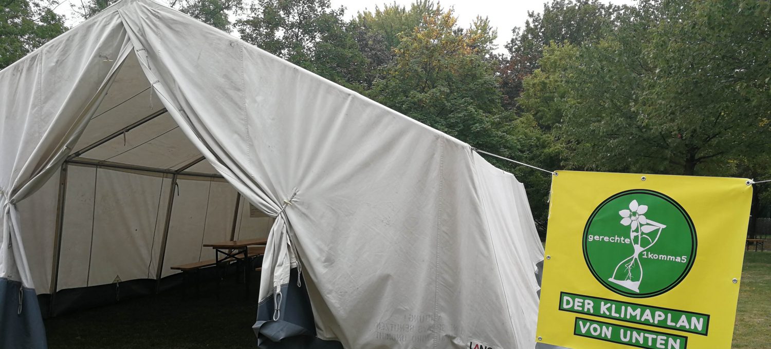 Zelt auf dem We4FutureCamp. Daneben ein gelbes Plakat mit Sanduhr und Klimaplan von unten