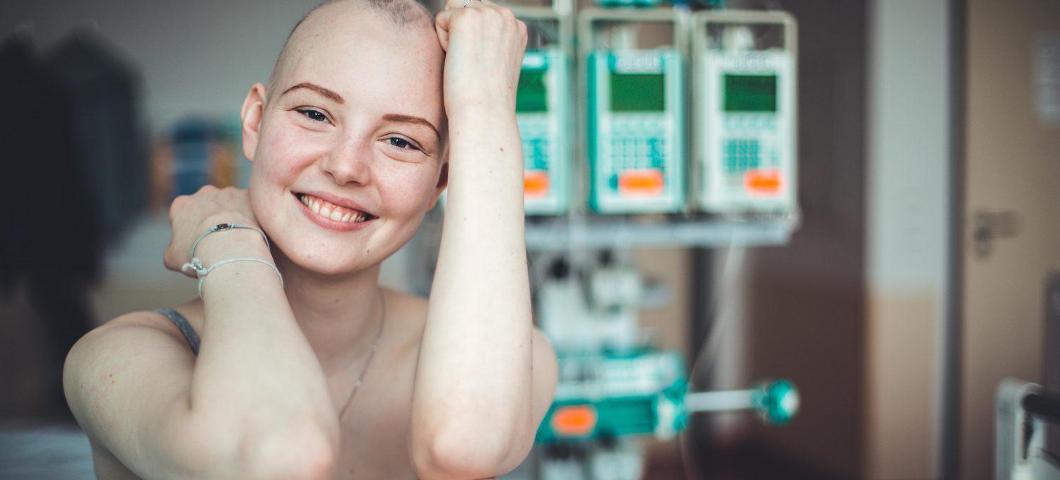 Mädchen mit Glatze sitzt vor Geräten im Krankenhaus und lächelt